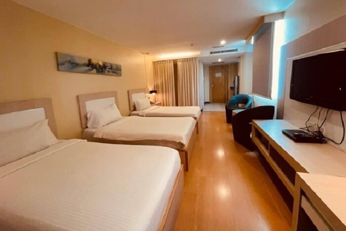Une chambre d’hôtel avec deux lits, un bureau avec un ordinateur, une télévision et un tableau au mur.