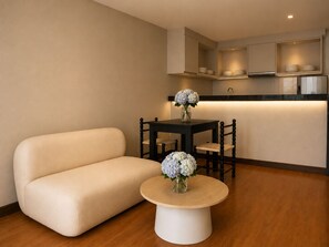 A modern kitchen with built-in cabinets, a dining table with chairs, a sofa, and a coffee table with flowers. - Blanco Apartment Hotel (Bintulu)