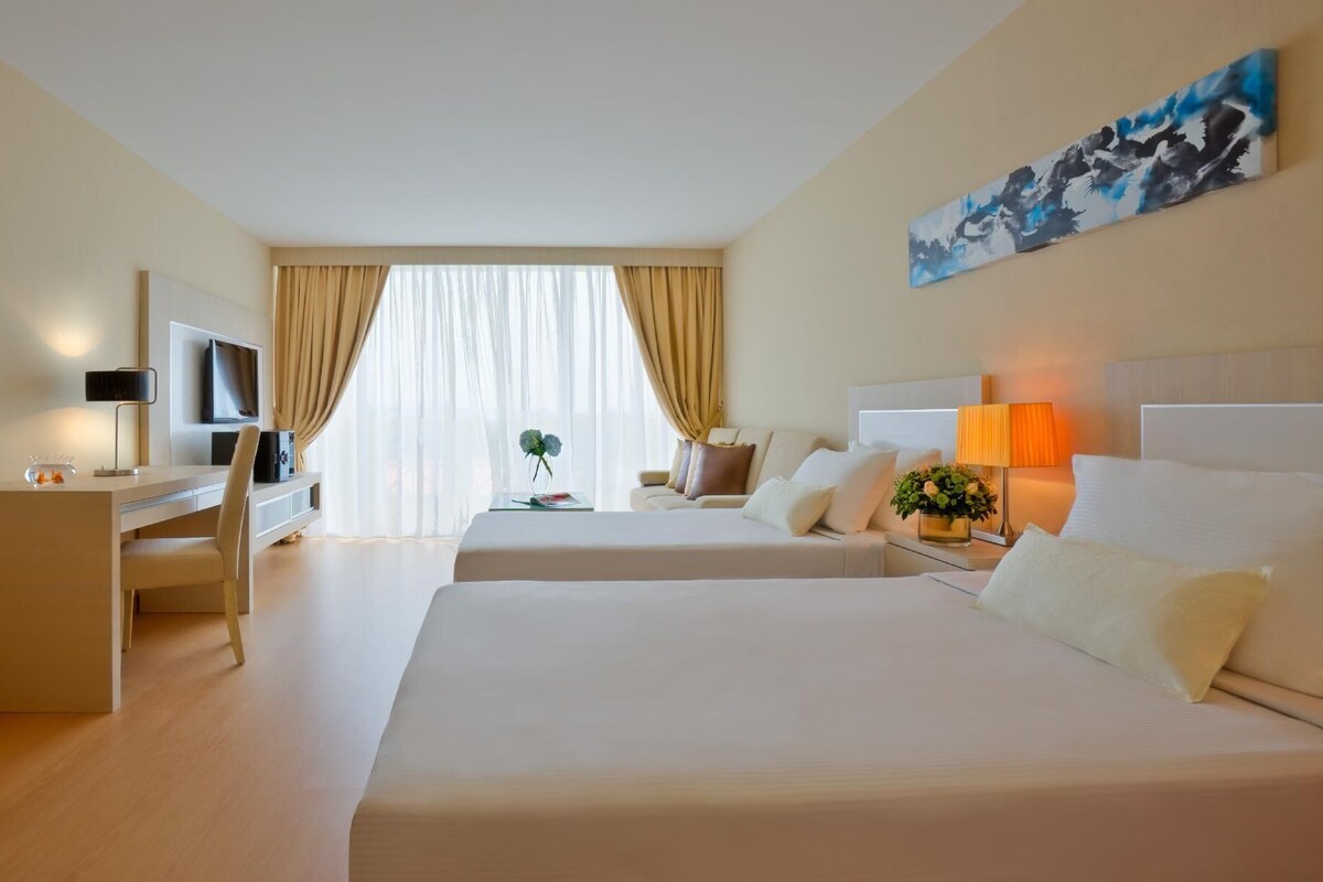 Ein Hotelzimmer mit einem großen Bett, einem Schreibtisch mit Fernseher, einem Sessel, einer Couch und einem Bild an der Wand.