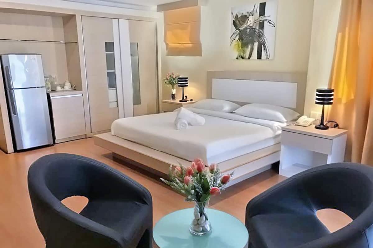 Une chambre d’hôtel comprenant un lit, des tables de chevet, un réfrigérateur, une petite table avec un vase de fleurs et deux chaises.