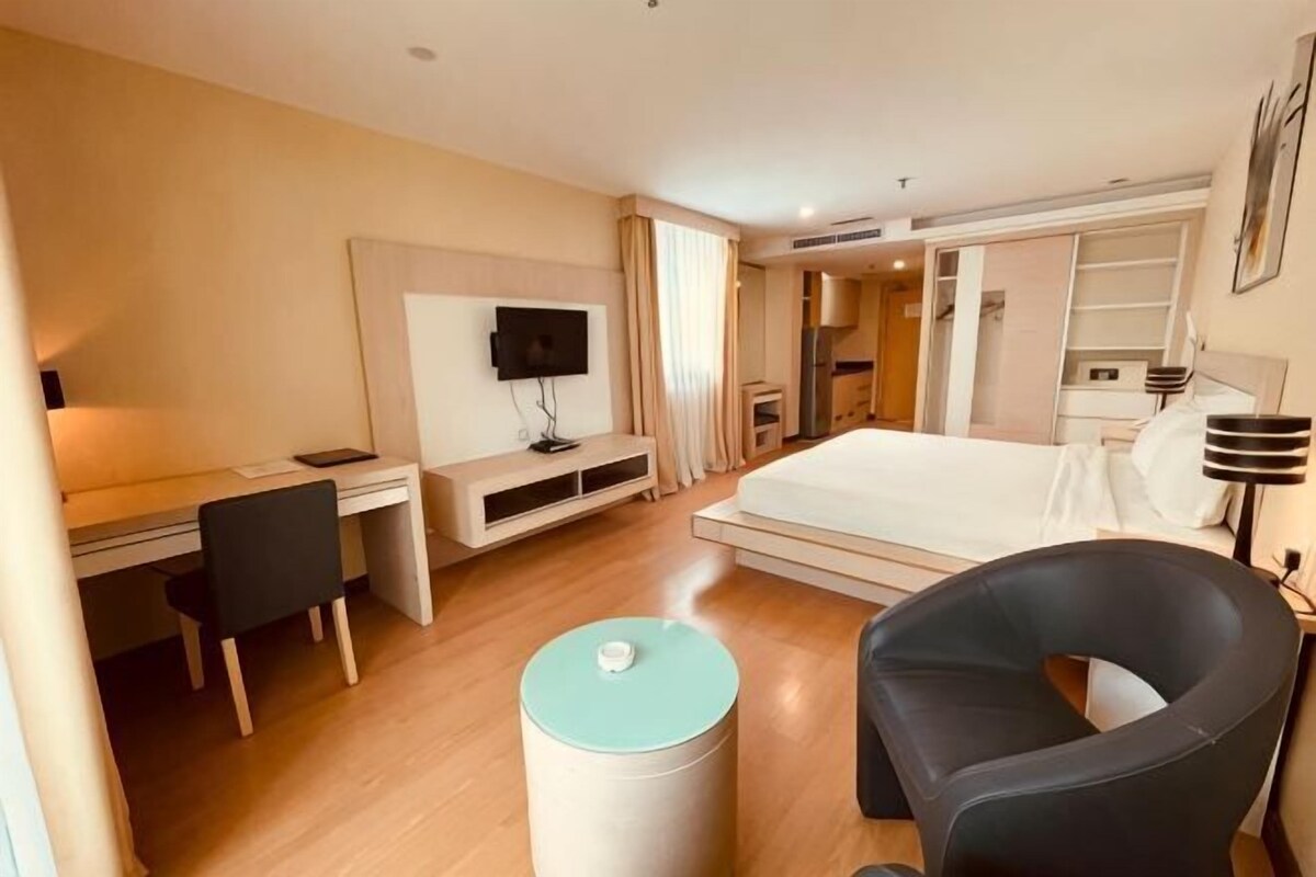A hotel room with a bed, desk, chair, TV, and a small table.