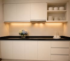 Una cocina con armarios blancos, encimera negra y un florero con flores.