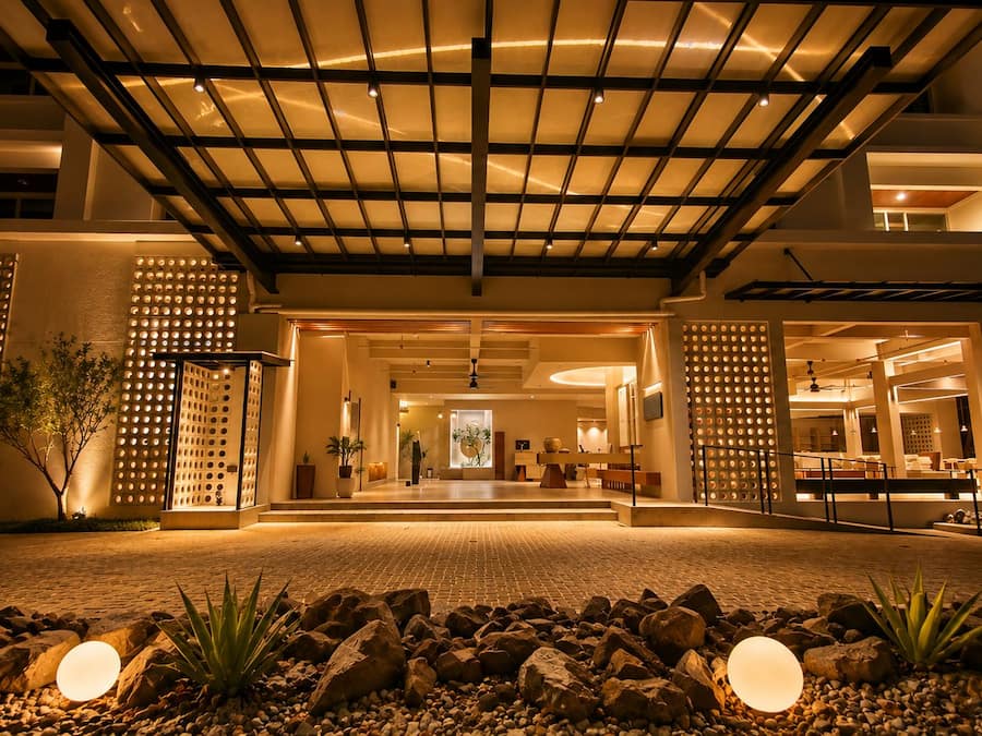 L’entrée d’un hôtel, avec un passage couvert, des plantes en pot et un espace d’accueil.