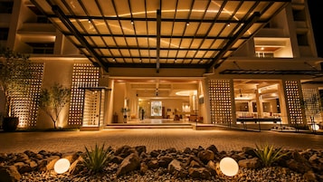 Entrada de hotel con un corredor cubierto, plantas en macetas y una zona de recepción.