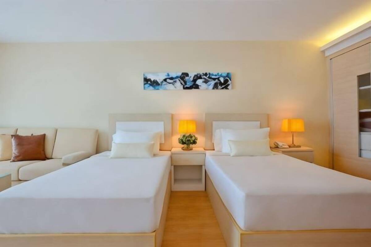 Une chambre d’hôtel avec deux lits, un canapé, une table de chevet avec une lampe et un tableau au mur.