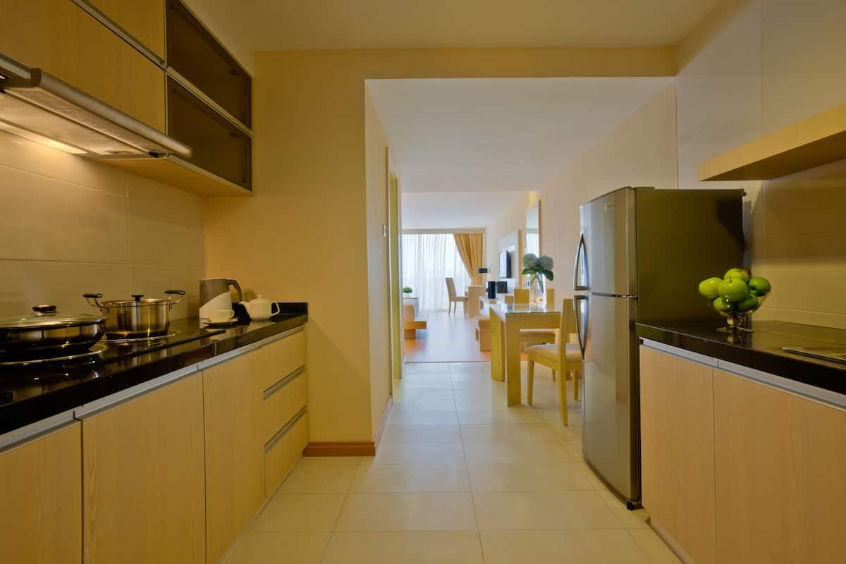 Une cuisine moderne avec des meubles en bois, un réfrigérateur en acier inoxydable et un coin repas à l’arrière-plan.