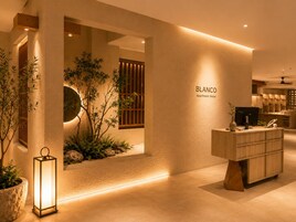 Un hall de hotel con una recepción, un cartel en la pared que dice 'BLANCO Apartment Hotel' y un pequeño jardín interior.