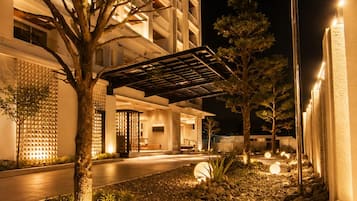 A nighttime view of a building with a landscaped area featuring a tree, rocks, and a spherical light.