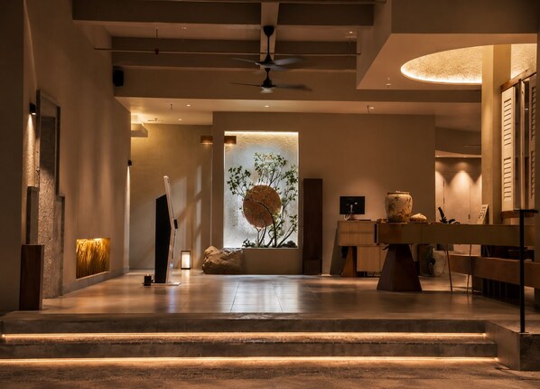 Un intérieur moderne agrémenté d’un élément décoratif central en eau, d’un ventilateur de plafond et d’un comptoir d’accueil.