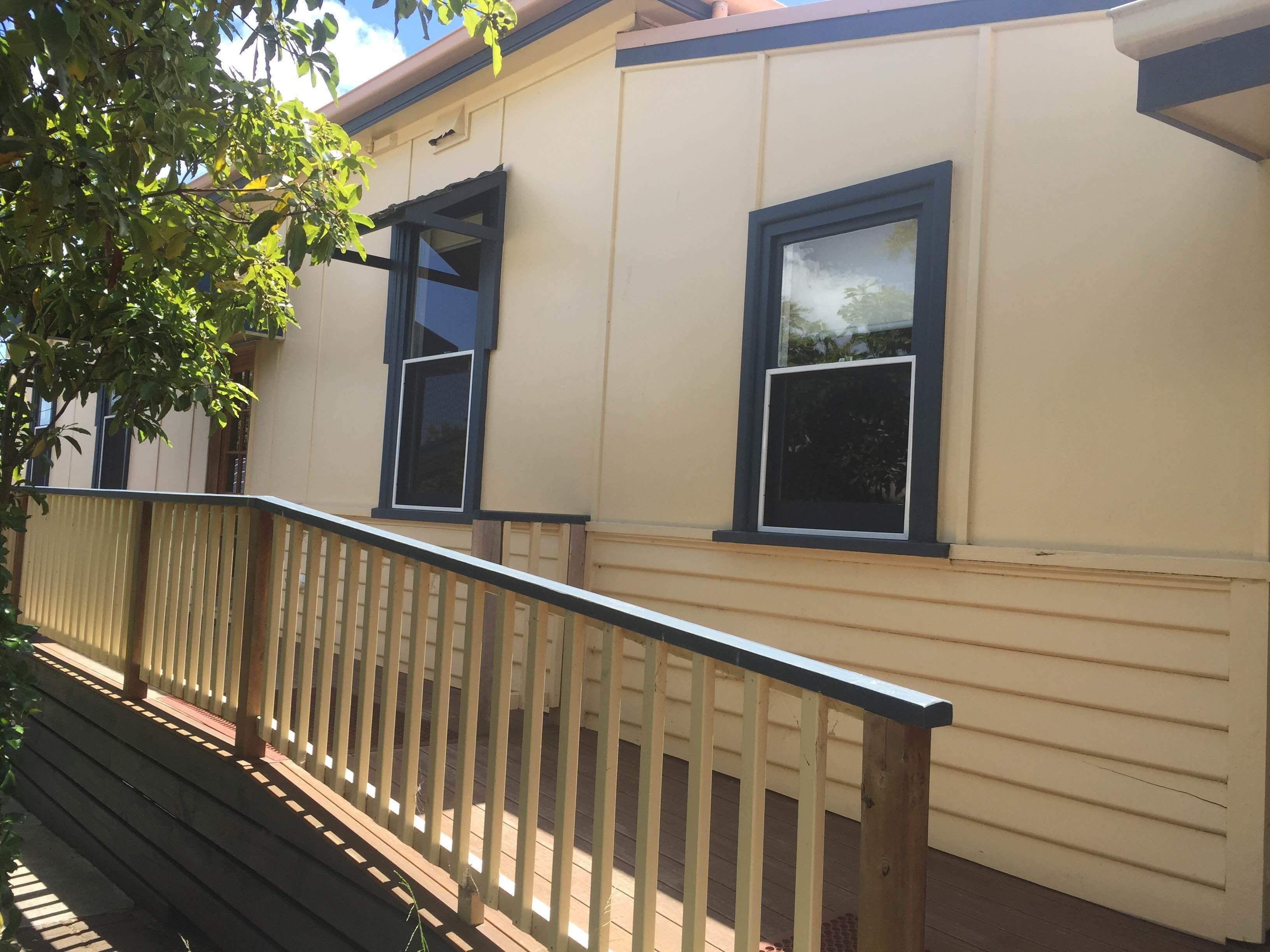 A building with two windows, a balcony with a wooden railing, and a tree in the foreground.