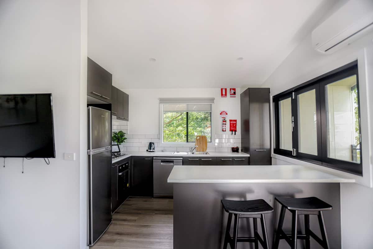A modern kitchen with a central island, bar stools, a built-in oven, and a window overlooking greenery.