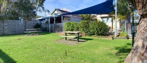 Un patio trasero con césped, una mesa de picnic y una vela de sombra azul.