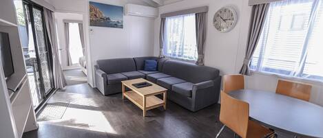 Uma sala de estar moderna com um sofá seccional, uma mesa de centro de madeira e uma área de jantar com mesa branca e cadeiras de madeira.