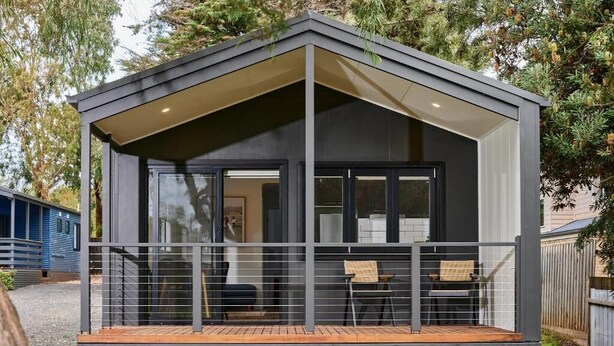 Een moderne, donkere cabin met een overdekte veranda, een houten terras en een glazen deur die naar de binnenkant leidt.