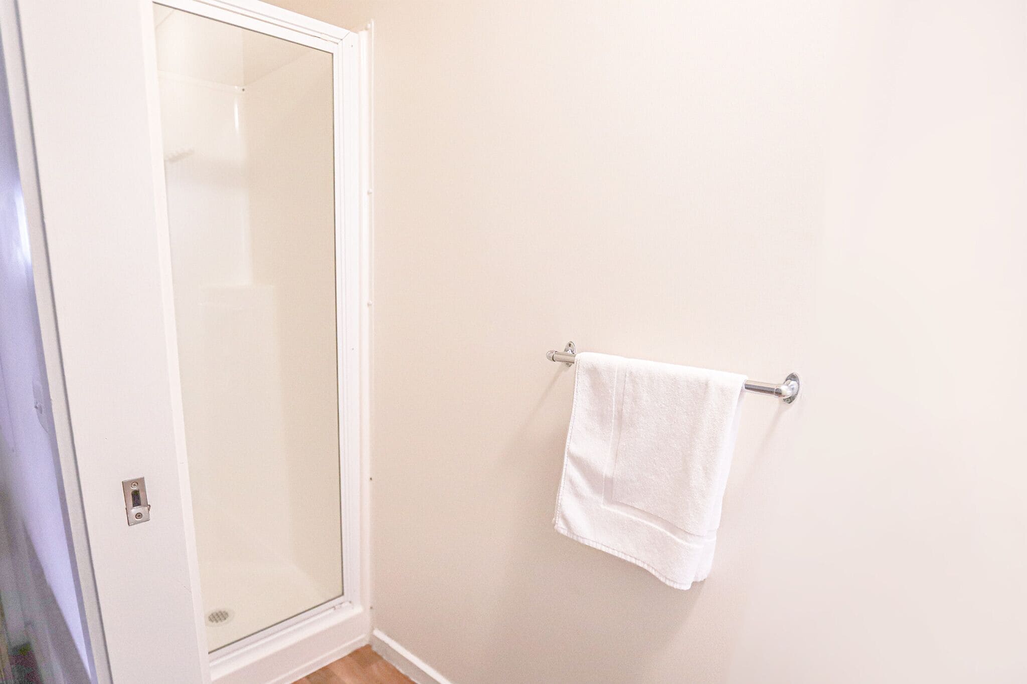 Ein Badezimmer mit Duschabtür aus Glas, einem weißen Handtuch an einer Metallhandtuchstange und einer schlichten Wand.