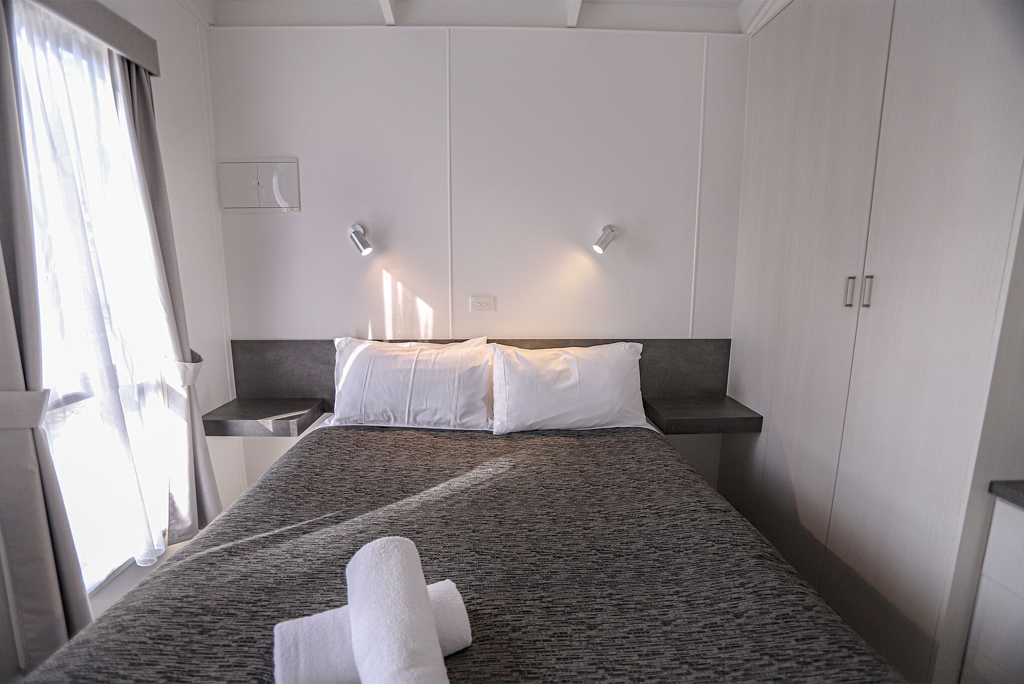 Una habitación de hotel con una cama grande, dos mesitas de noche, un armario y una ventana con cortinas.
