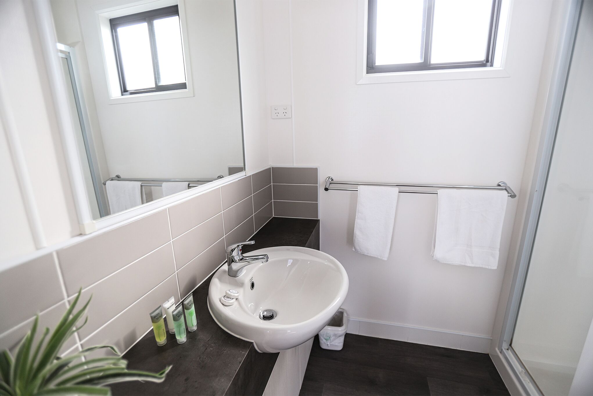 Ein modernes Badezimmer mit einem weißen Waschbecken, zwei Handtuchhaltern und einem Fenster.