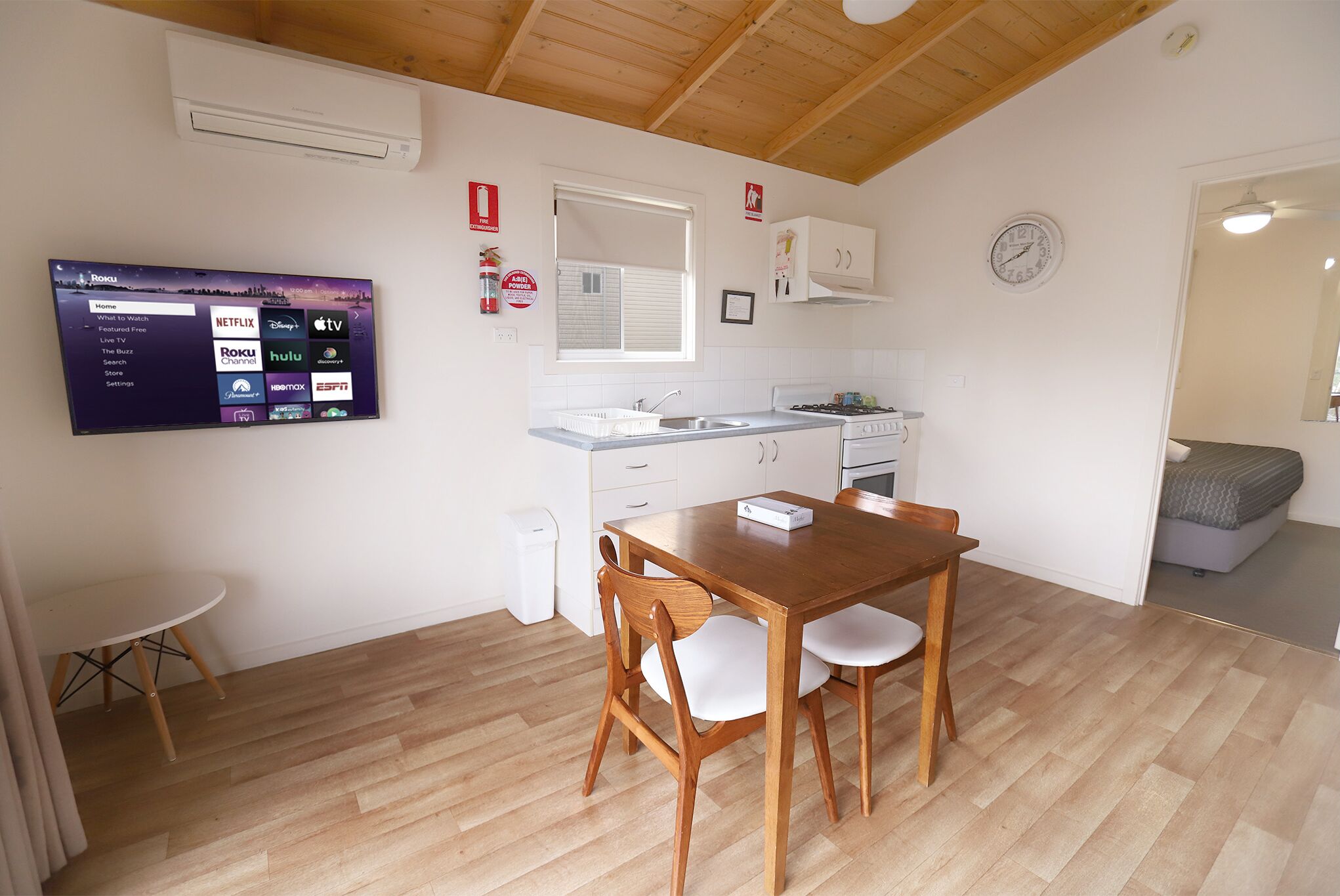 A compact kitchen with a wooden table and chairs, a built-in oven, and a wall-mounted TV displaying streaming services.