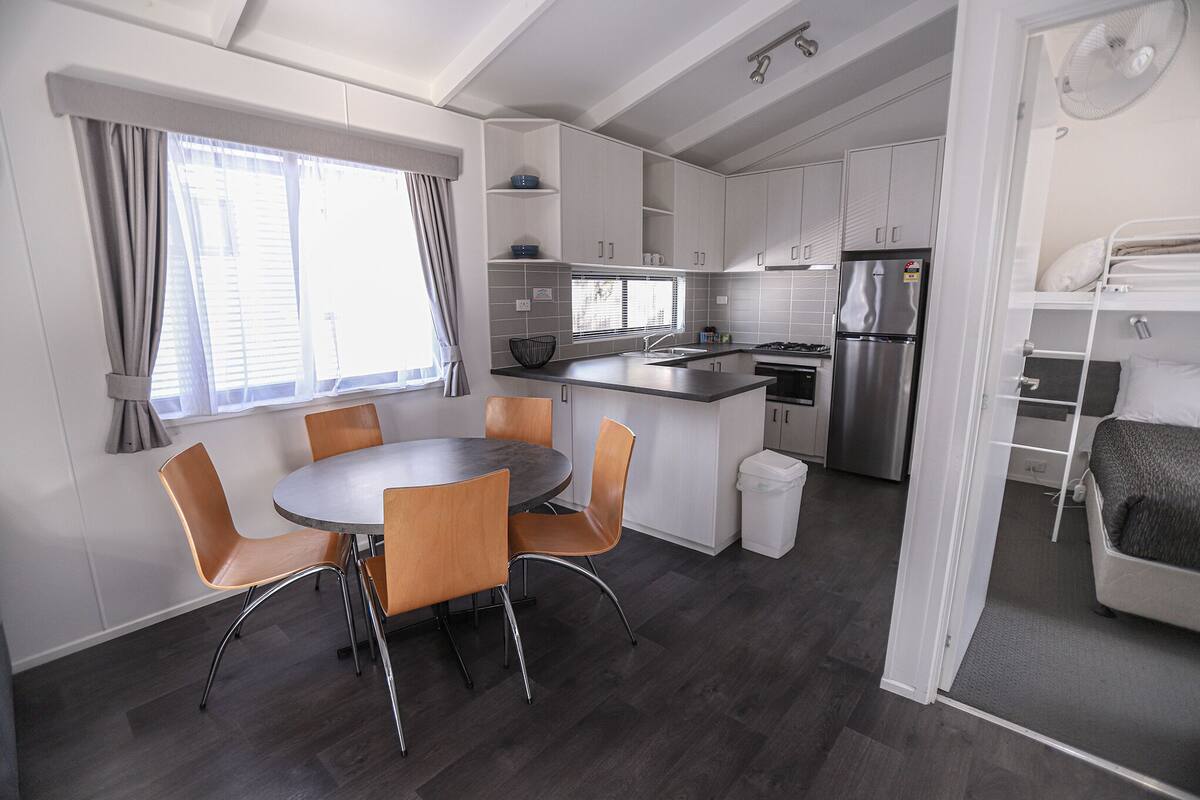 A compact kitchen with a dining area, built-in cabinets, a refrigerator, and a window with curtains.