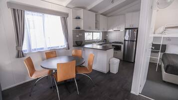 A compact kitchen with a dining area, built-in cabinets, a refrigerator, and a window with curtains.
