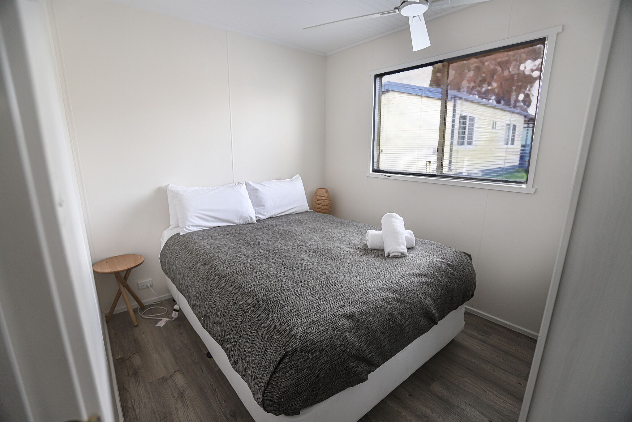 A bedroom with a bed, a small side table, a window with blinds, and a ceiling fan.