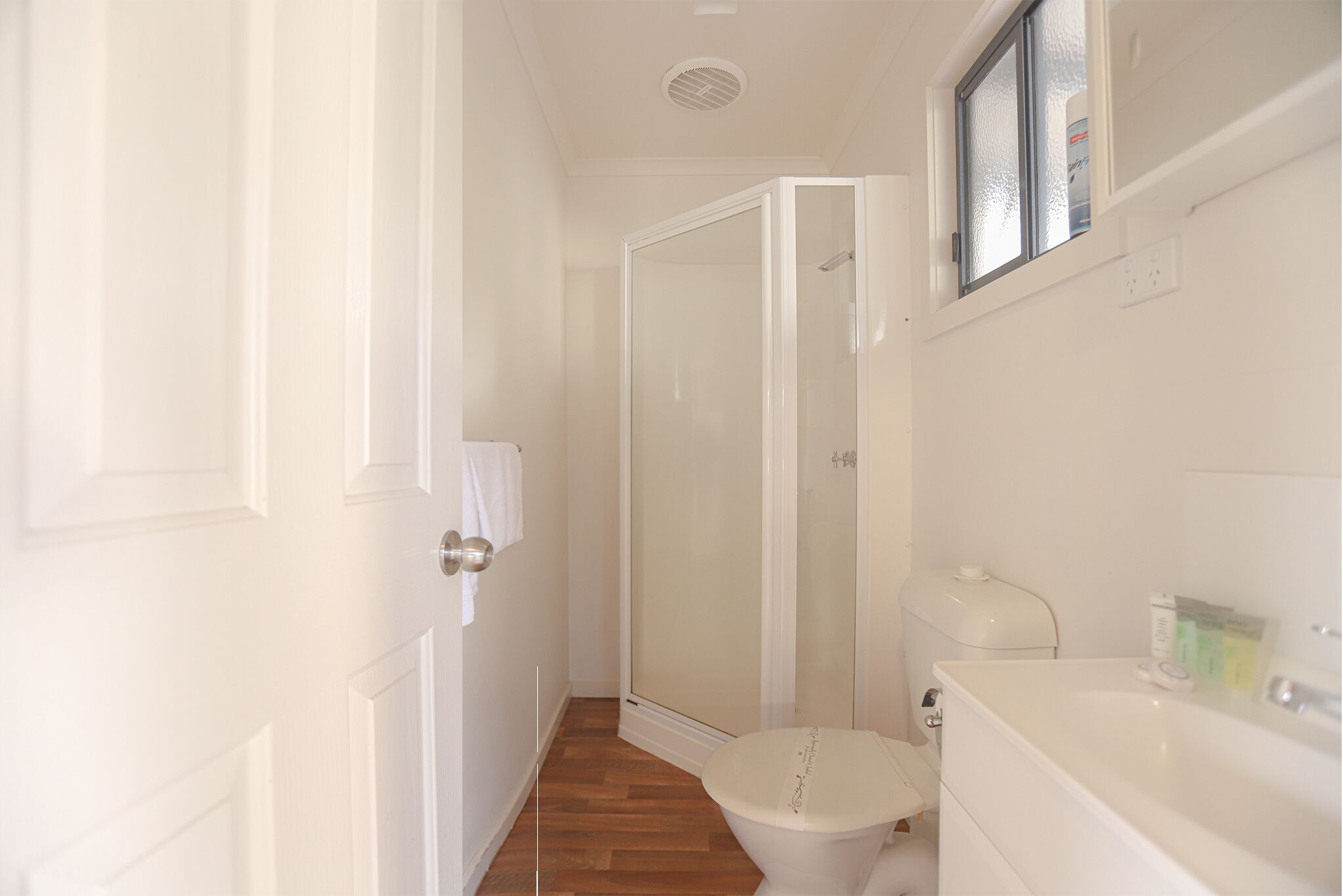 A narrow bathroom with a toilet, a shower enclosure, and a sink.