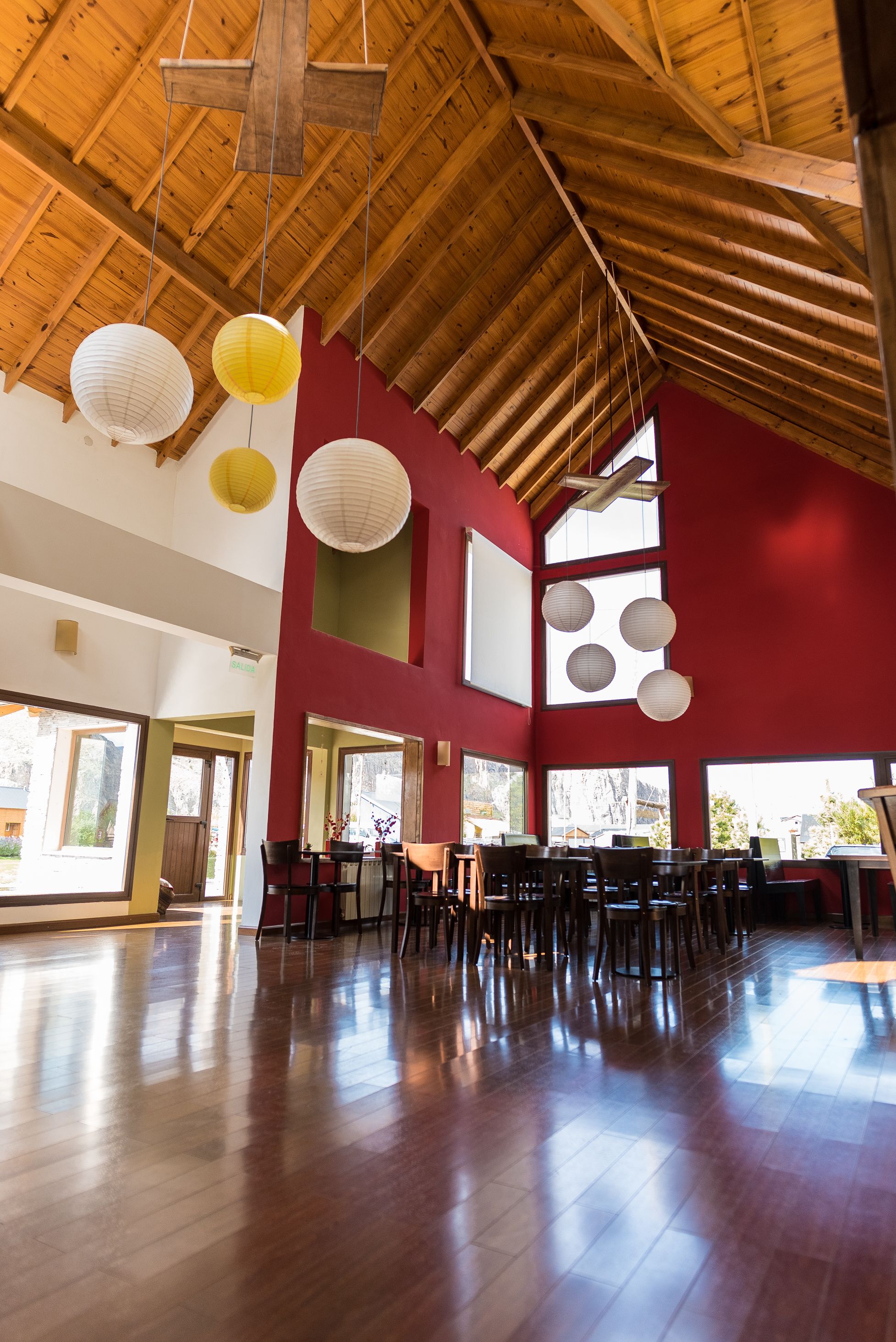 A spacious interior with a high wooden ceiling, large windows, and a red accent wall.