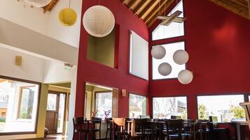 A spacious interior with a high wooden ceiling, large windows, and a red accent wall.