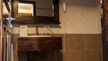 Un baño con tocador de madera, un espejo, secador de pelo, lavamanos y un inodoro.