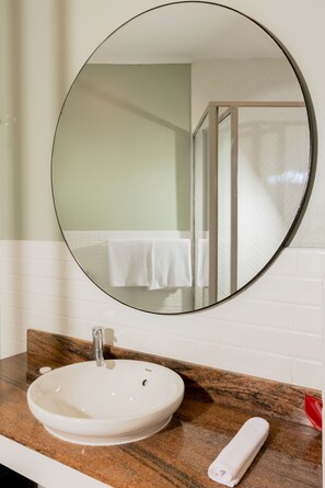 A bathroom with a round mirror, a white sink, and a towel on the counter. - Capricorn Hotel Suva (Suva)