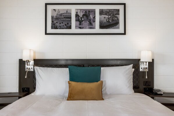A neatly made bed with white and teal pillows, a brown accent pillow, and a framed picture above. - Capricorn Hotel Suva (Suva)