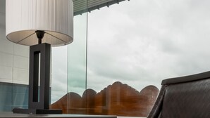 Una habitación moderna con un sillón de cuero negro, una mesa con lámpara y vistas a montañas a través de un ventanal.