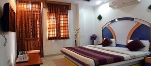 A bedroom with a bed, curtains, a bedside table, and a wall-mounted air conditioner. - Anoop Hotel (New Delhi)