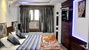 Een hotelkamer met een bed, een televisie, een plafondventilator, een raam met gordijnen en een wandairconditioning.