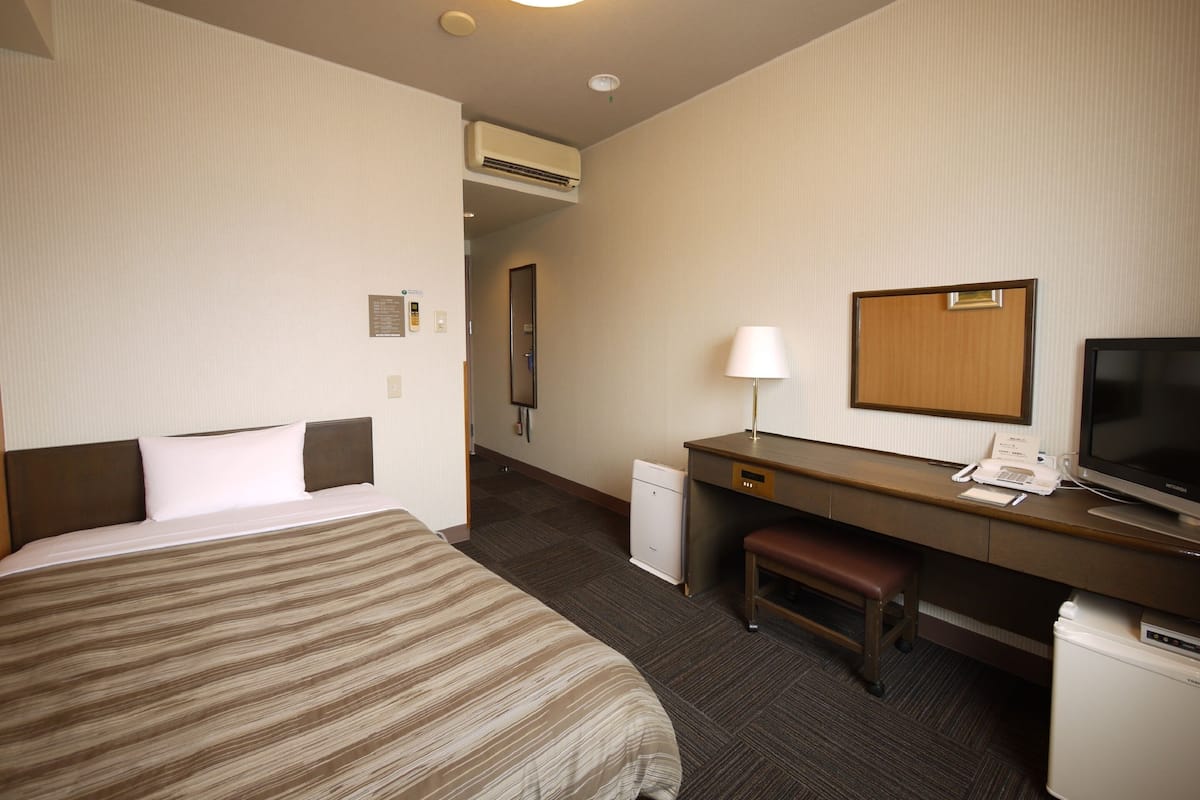 A hotel room with a bed, desk, chair, television, and a small refrigerator.