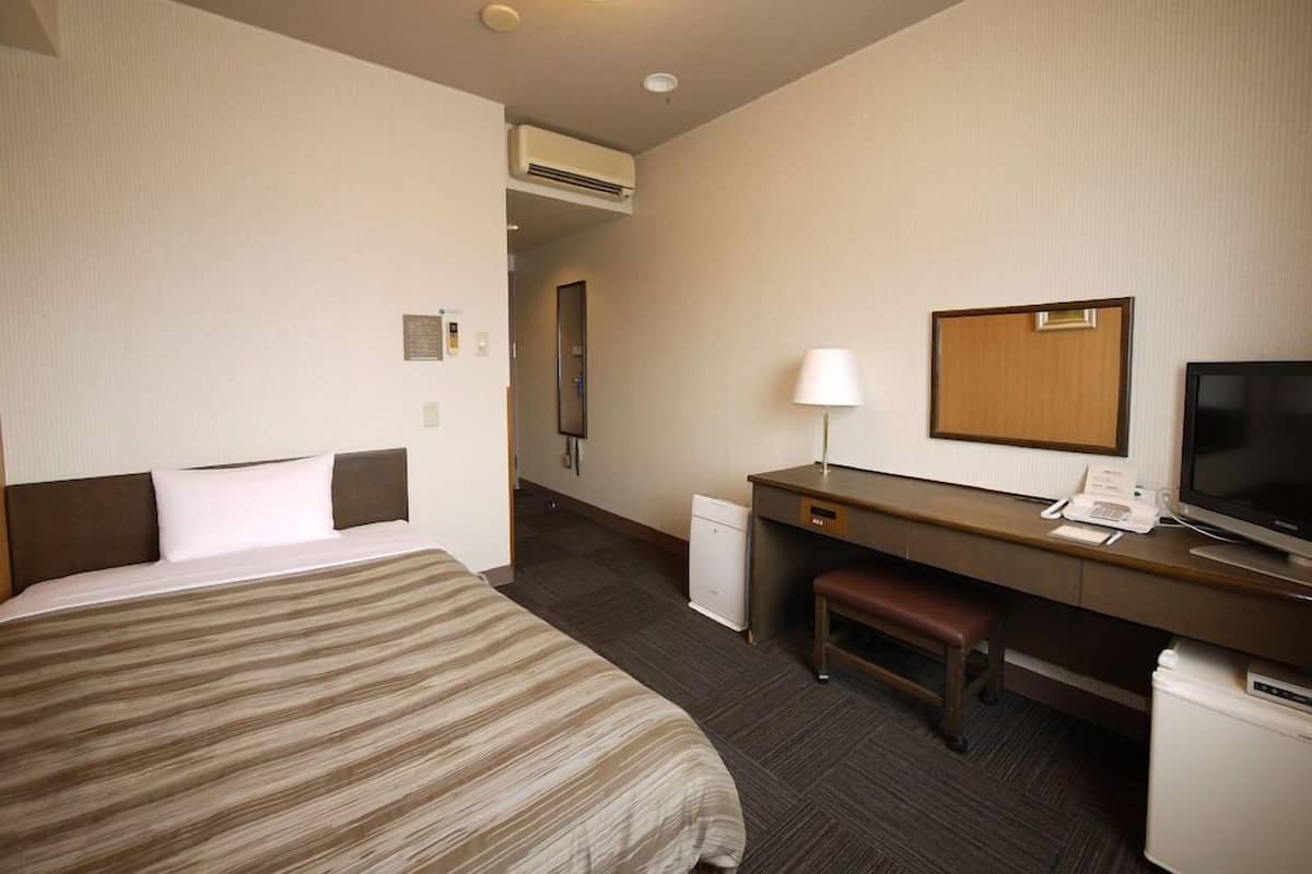 A hotel room with a bed, desk, chair, television, and a small refrigerator.
