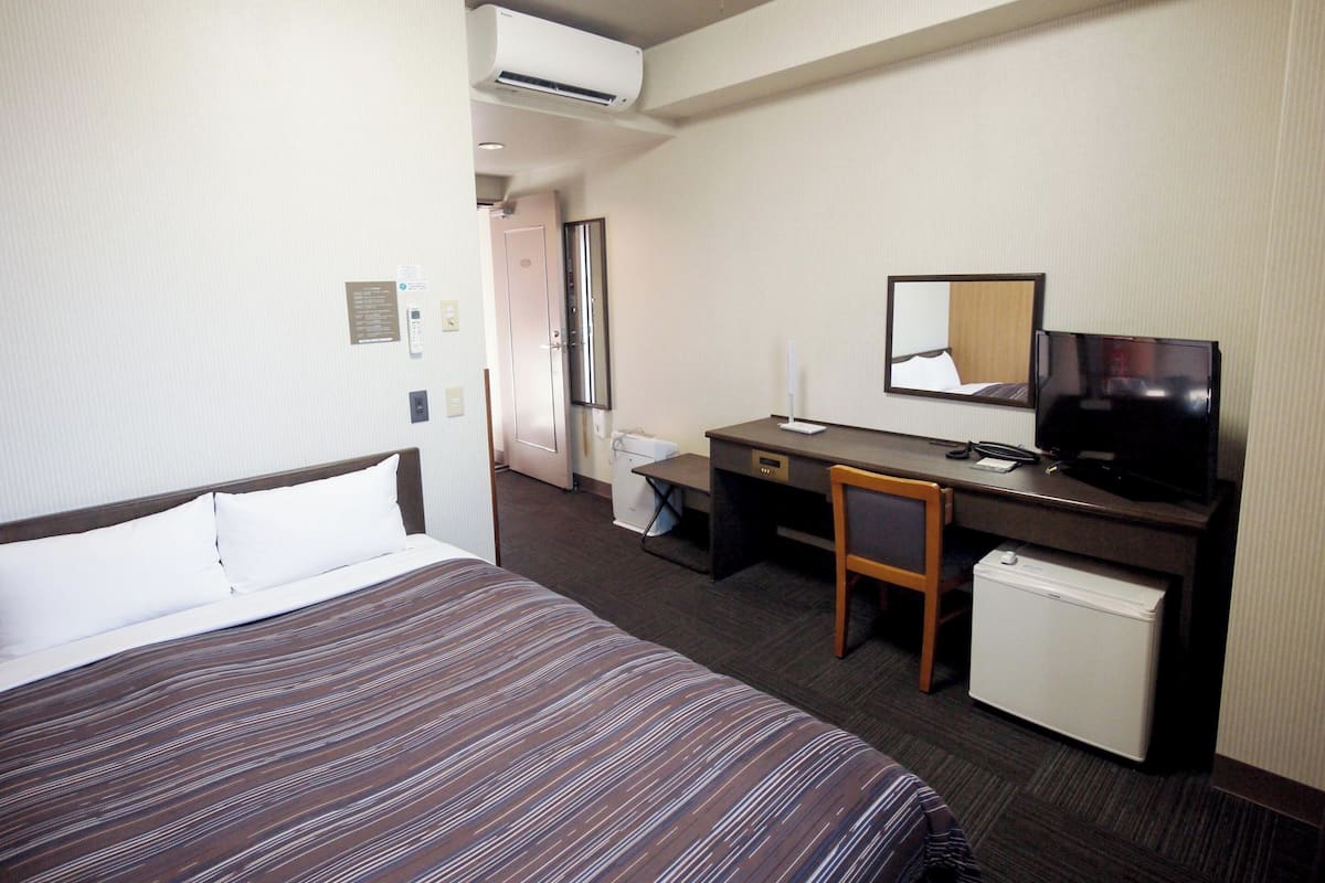 A hotel room with a bed, a desk with a chair, a television, and a small refrigerator.