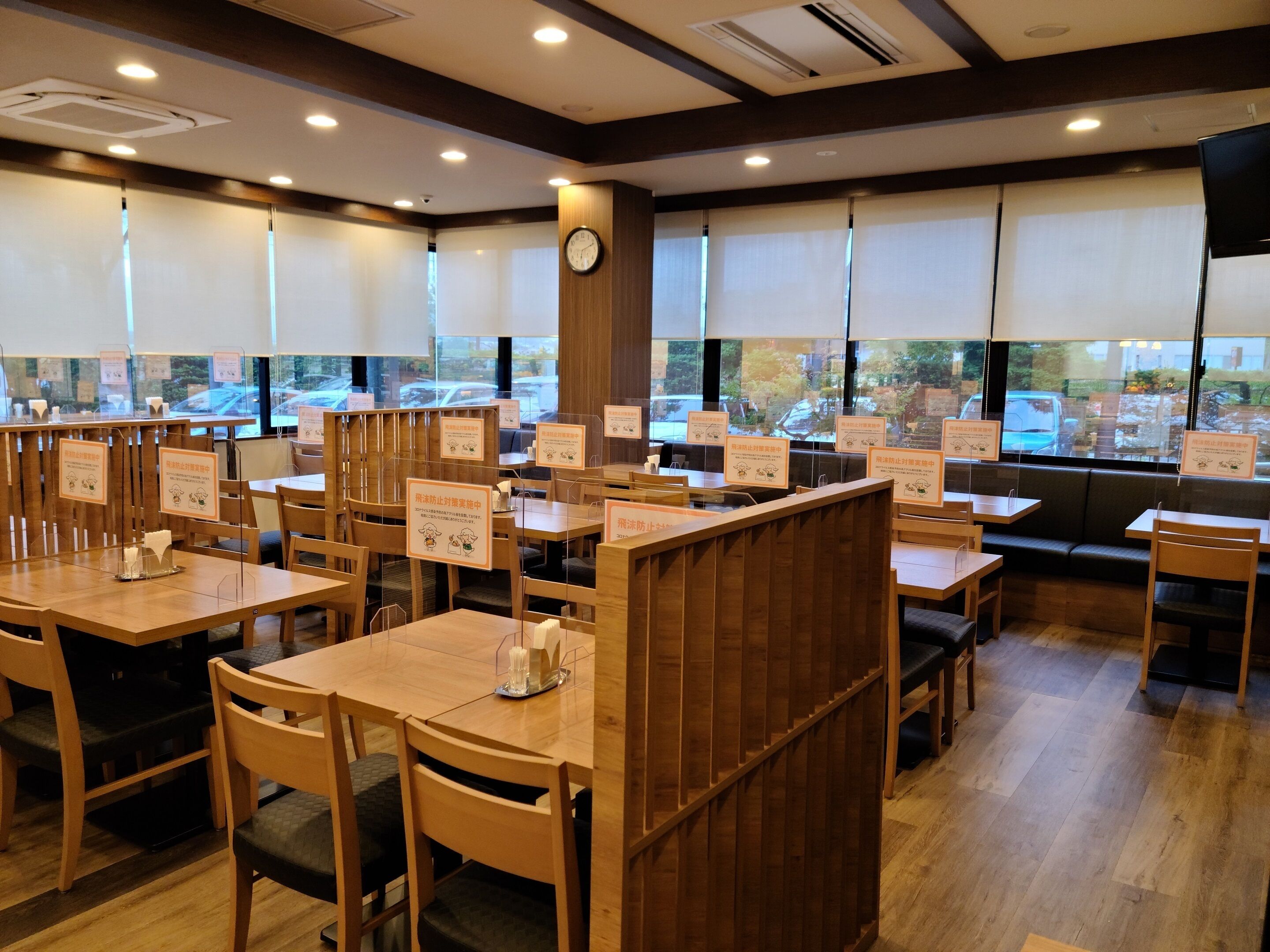 Interior de restaurante con mesas y sillas de madera, separadores transparentes y señalizaciones con ilustraciones.