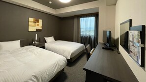Habitación de hotel con dos camas, un escritorio con televisor, una ventana con cortinas e iluminación en el techo.