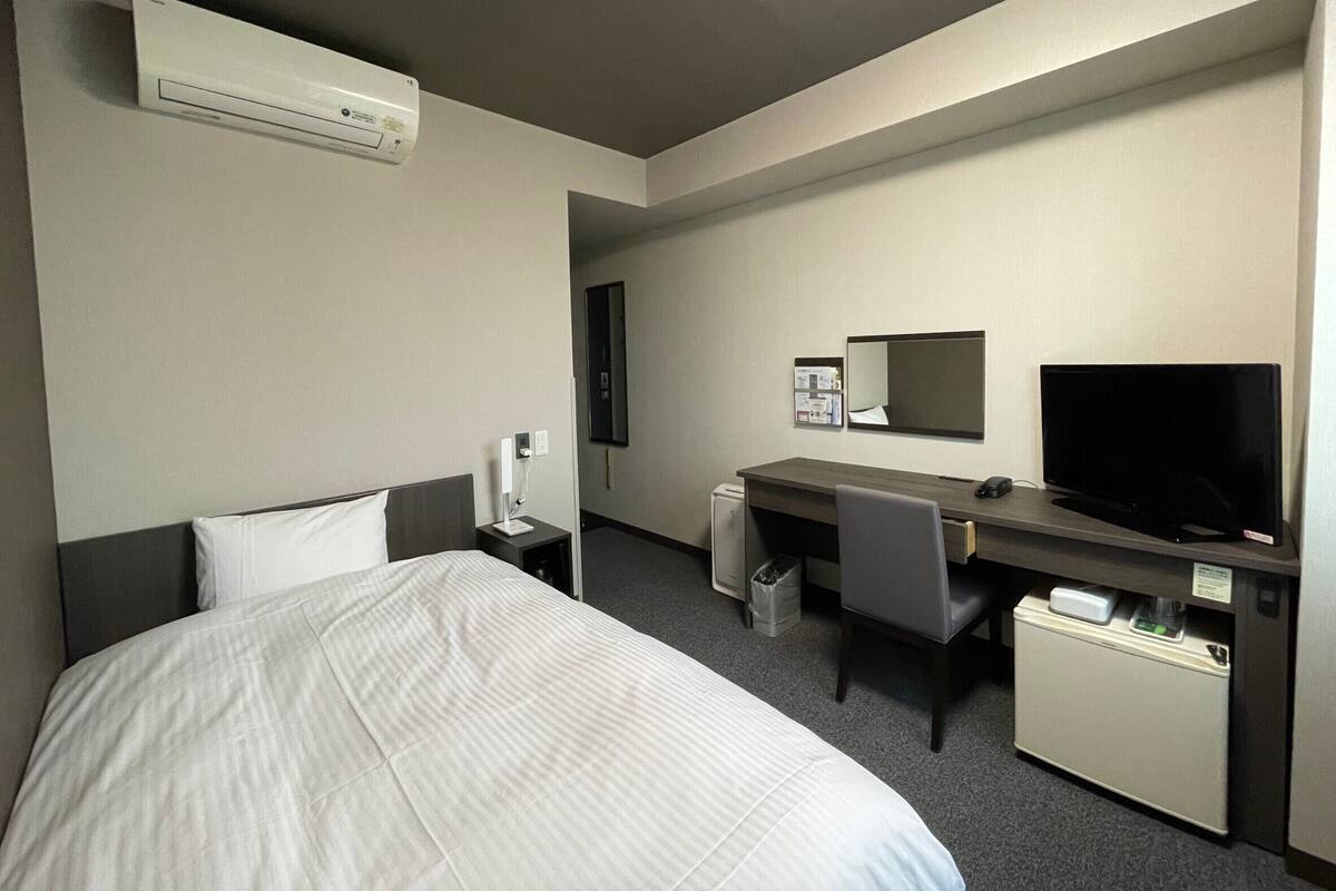 A hotel room with a bed, a desk, a television, and a small refrigerator.