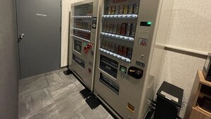 Una máquina expendedora con diferentes bebidas y aperitivos, una puerta para personal autorizado y un cubo de basura.