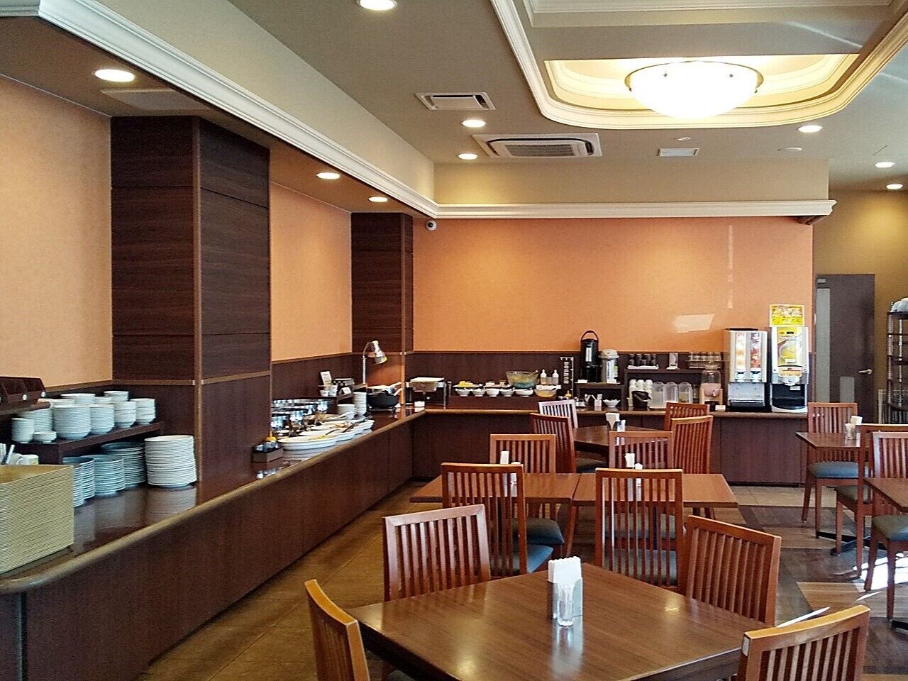 Een restaurant met houten tafels en stoelen, een buffet met borden en kommen, en een koffieapparaat.