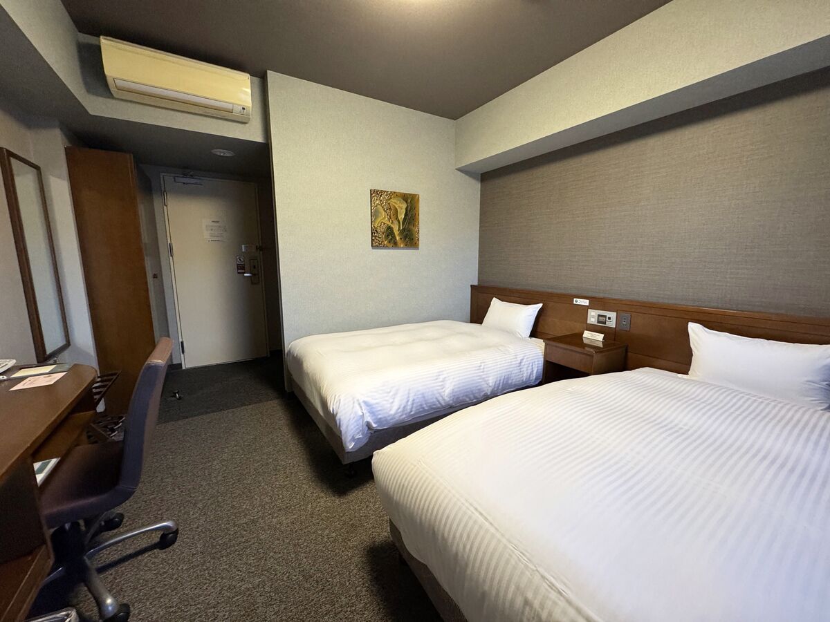 A hotel room with two beds, a desk, a chair, and a painting on the wall.