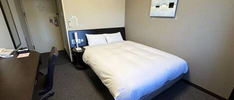Habitación de hotel con cama, escritorio, silla, mesita de noche, teléfono y un cuadro en la pared.