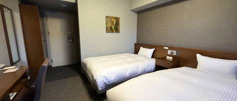 A hotel room with two single beds, a desk with a chair, an air conditioning unit, and a door leading to another room.