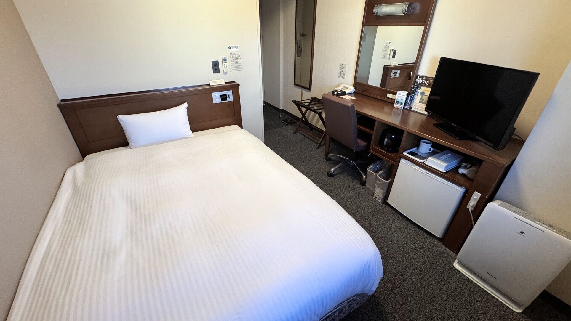 A hotel room with a bed, a desk, a television, a mini-fridge, and a microwave.