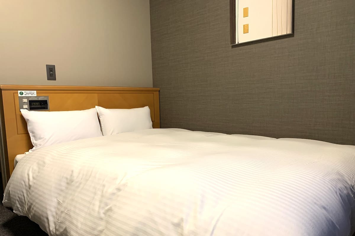 Une chambre d’hôtel équipée d’un lit, d’un panneau de commande et d’un luminaire fixé au mur.