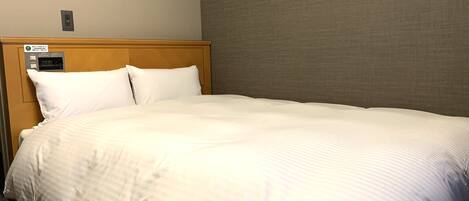 A hotel room with a bed, a control panel, and a wall-mounted light fixture.