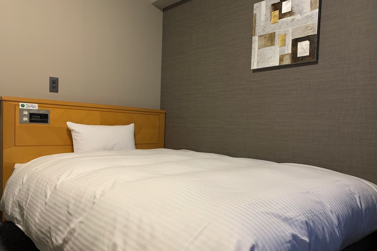Une chambre d’hôtel avec une tête de lit en bois, une couvre-lit blanche et une œuvre d’art accrochée au mur.