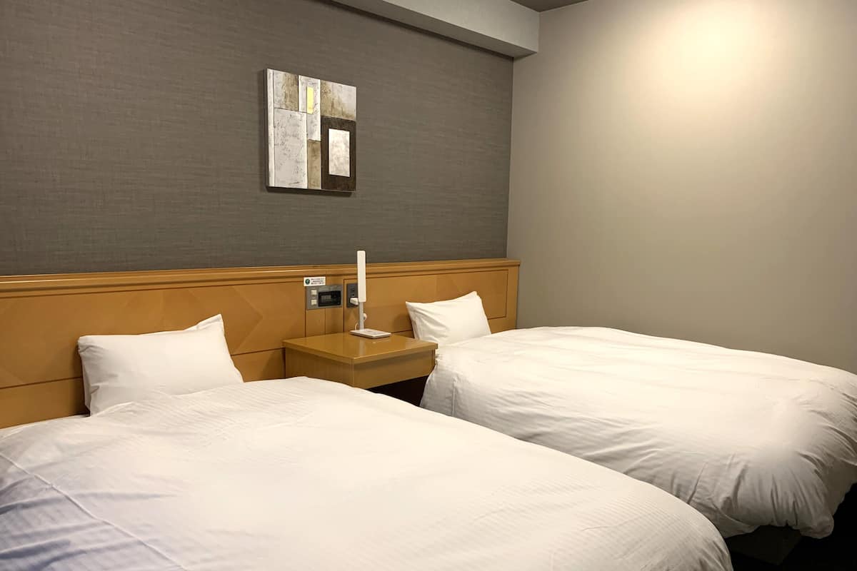 Une chambre d’hôtel avec deux lits, une table de chevet, une lampe et un miroir fixé au mur.